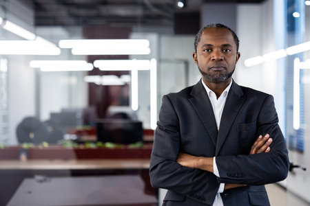 Confident businessman standing with arms crossed in modern office environment. Image emphasizes leadership, professionalism, and serious demeanor in contemporary workspace.の写真素材