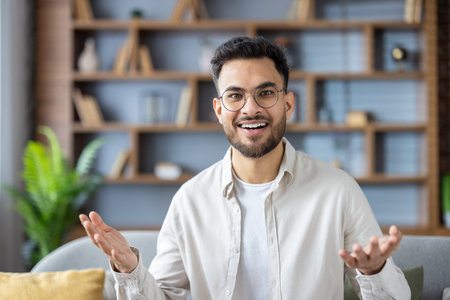 Close-up portrait of a young Indian man sitting on the couch at home and talking smiling at the...