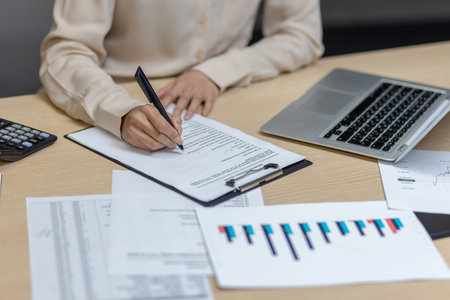 Hispanic businesswoman at office desk analyzing financial documents with laptop and calculator....