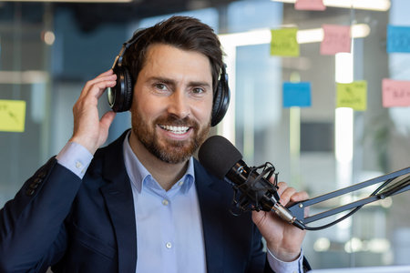 Confident man wearing headphones using microphone for podcast recording in office setting portrays...