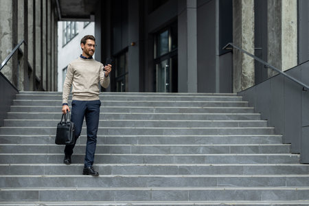 Serious man descends stairs in city while using phone. He wears business attire and carries briefcase, exhibiting focused and professional demeanor.の写真素材