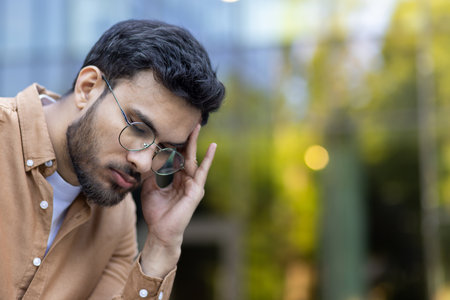 Young man wearing glasses with hand to head showing stress and contemplation. Personality captured in thoughtful moment, reflecting feelings of concern or anxiety.の写真素材