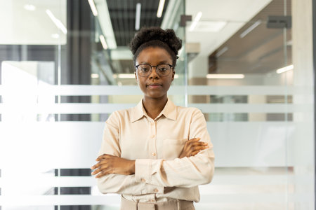 Confident African American businesswoman standing with arms crossed in modern office. Portrays leadership, confidence, and professionalism. Ideal for depicting successful business environmentの写真素材