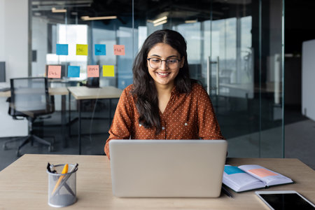 Young beautiful woman working inside office with laptop, business woman typing on keyboard, happy smiling satisfied with work result at workplace, company employee.の写真素材