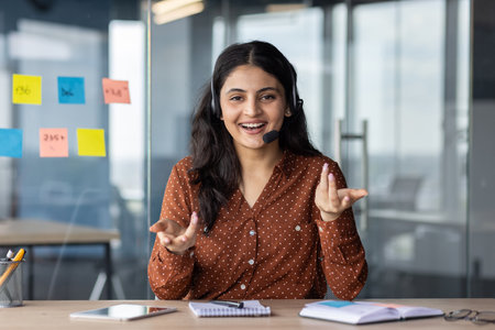 Webcam view, video call online meeting, woman with headset phone smiling and looking at camera, talking remotely with clients and colleagues, business woman at workplace inside office.の写真素材