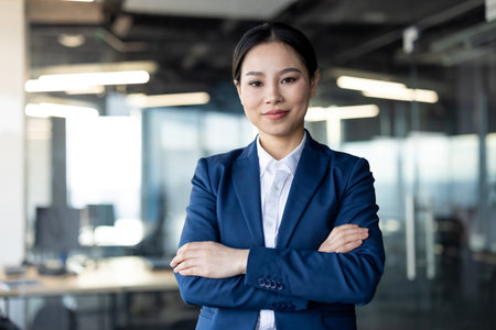 Confident asian businesswoman with arms crossed in modern office. Professional attire conveys leadership and success. Bright office environment emphasizes successful career imageの写真素材