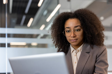 Close-up photo of a young African-American businesswoman sitting in an office in a business suit and concentrating on a laptop.の写真素材