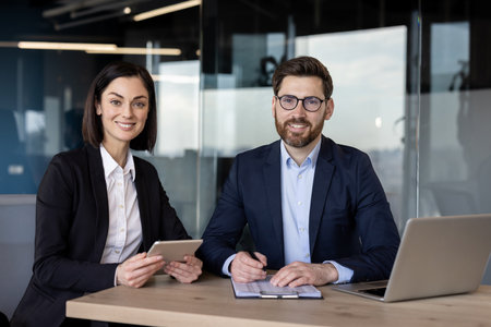 Business professionals collaborating on digital tablet and documents in modern office. Man and woman engaged in project discussion, showcasing teamwork and leadership skills with technologyの写真素材