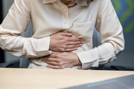 Office worker clutching stomach indicating pain or discomfort, possibly due to indigestion or stress within professional environment. Image suggests health issue faced by employees during work.の写真素材