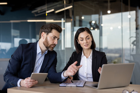 Business colleagues engaged in discussion over project ideas. Man holding tablet , woman pointing at laptop screen. Collaborative teamwork in modern office environment focused on planning strategy.の写真素材