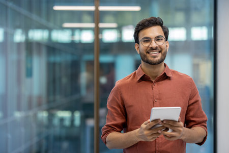 Smiling businessman holding tablet in office setting conveys confidence and engagement with technology. Professional environment highlights modern workplace dynamics and success.の写真素材