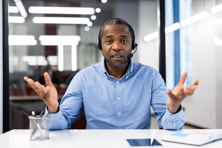 Confident professional man wearing headset participates in video call. Expressive gestures convey...