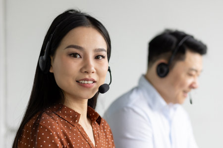 Asian customer service representatives focused on providing excellent support in office environment. Headset communication for efficient service. Teamwork and professionalism emphasized in workplaceの写真素材