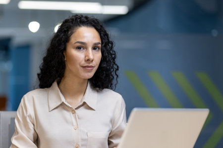Confident woman working at laptop in modern office. Demonstrating focus, determination, professionalism. Ideal for business, workspace, or career concepts.の写真素材