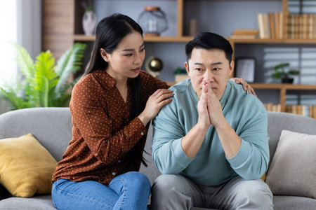 Asian couple sitting on sofa, woman comforting man, showing support, empathy, understanding....