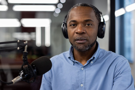 Mature African American male businessman with headphones, microphone in modern studio, engaged in...