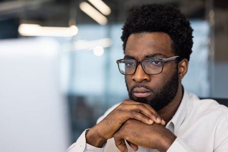 African American man businessman intensely focused on computer in office. Wearing glasses,...