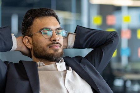 A mature businessman relaxing confidently in corporate office space. Wearing business attire, he demonstrates a calm and serene expression, embodying professionalism and success in a workplaceの写真素材