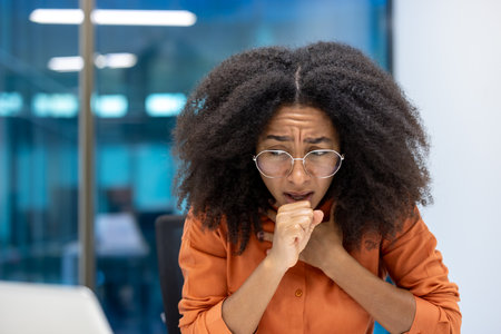 Sick woman coughing at workplace, unhealthy businesswoman close up with cold, sick with flu, working inside office building.の写真素材