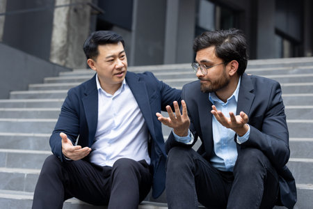 Supporting and comforting a partner, two men in business suits sitting on the stairs of an office building, a colleague helps a friend cope with frustration and anxiety.の写真素材