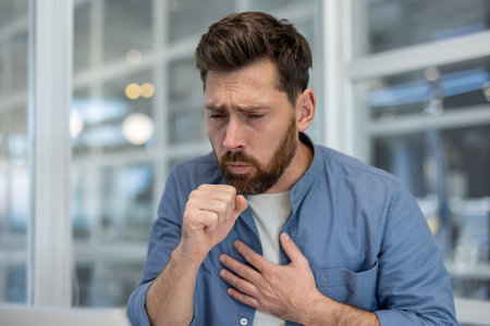 Sick coughing man close up. Office worker with cold at workplace in the middle of the office, got...