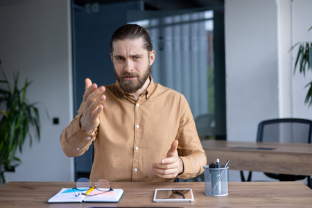 Professional businessman expressing opinions seated at desk in workspace. The setting includes...