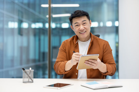 Individual with notebook at desk looking at camera, participating in online meeting and business conference remotely. Professional at workplace inside office setting.の写真素材
