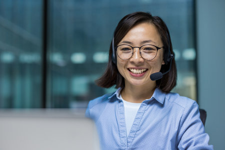 Asian Office worker with headset phone close up, woman working with laptop for video call, consulting customer customers sitting inside office at workplace.の写真素材