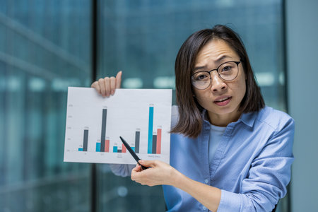 Webcam view, online business meeting remote conference presentation. Woman anxious and upset showing report graph with negative indicators. Asian financier inside office at workplace.の写真素材