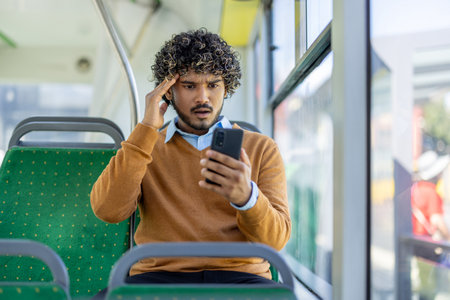 Upset man riding public transport, bus with phone in hand, reading news from smartphone app in frustration and anxiety.の写真素材