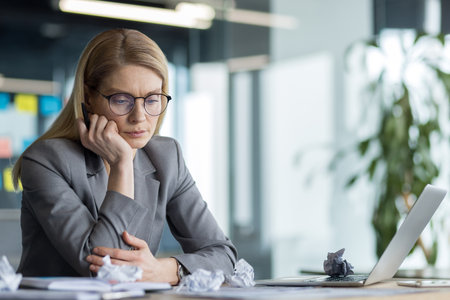 Sad worried woman sitting at her desk in a business suit among pieces of torn paper. Businesswoman failed, bankrupt, dissatisfied with the results of financial activities.の写真素材