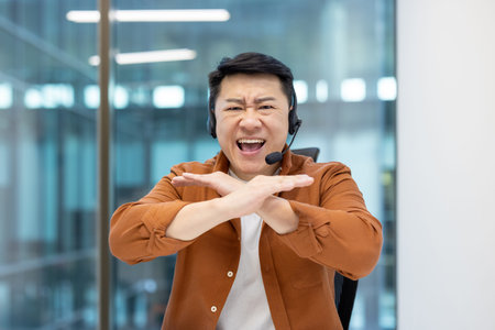 Webcam view, Asian man with headset quarreling, shouting at camera. Dissatisfied support worker cant...