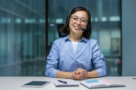 Webcam view, female support worker with headset smiling and looking at camera. Woman at workplace inside office, consulting and helping clients remotely online.の写真素材