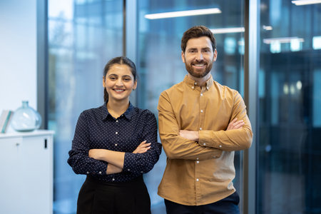 Smiling business professionals stand together with arms crossed in a bright, modern office setting, ready for success.の写真素材