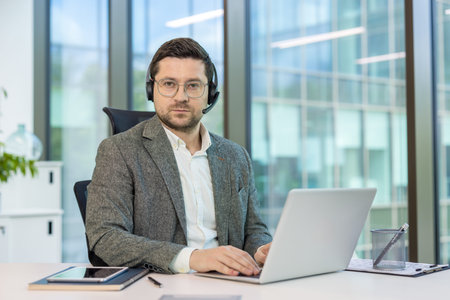 Serious young man, office worker and consultant sitting at desk, working on laptop and looking at...