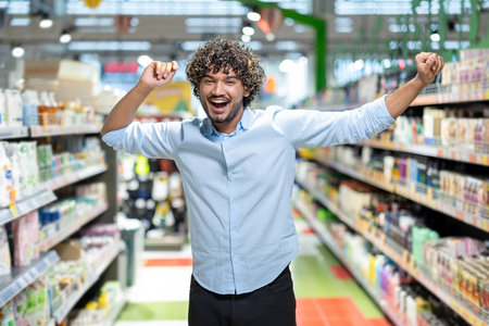 A joyful man celebrates his success in a supermarket, arms raised, expressing happiness. The stores interior is visible.の写真素材