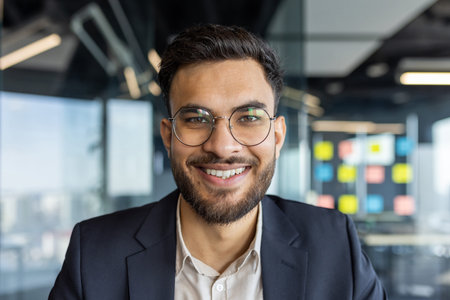 Portrait of successful young businessman at workplace inside office. Man smiling close up and...
