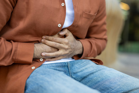 A man clutches his abdomen, suggesting abdominal discomfort or pain. The image highlights the pose,...
