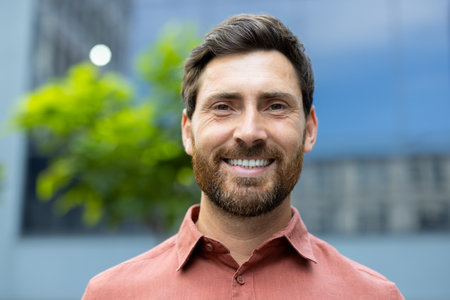 A handsome man smiles brightly, his eyes twinkling. Hes outdoors, looking directly at the camera, exuding warmth and approachability.の写真素材