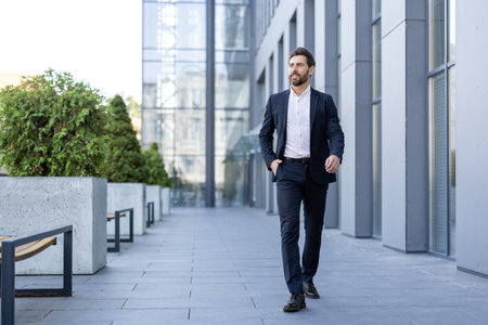 A well-dressed businessman walks confidently in a modern urban setting, exuding professional ambition. He is wearing a dark suit.の写真素材