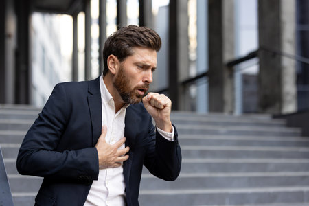 A man in a suit coughs and clutches his chest, appearing ill on outdoor steps.の写真素材