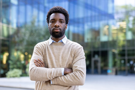 An African-American man stands confidently with arms crossed outside an office building. He looks at the camera with a serious expression.の写真素材