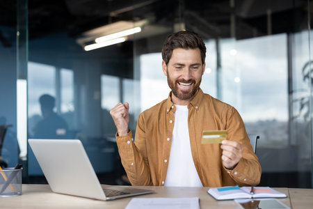 A man celebrates with a credit card near a laptop, showing excitement. The scene depicts online...