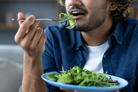 A close-up shows a man enjoying a healthy salad with a fork. Fresh greens on a blue plate enhance the view.の写真素材