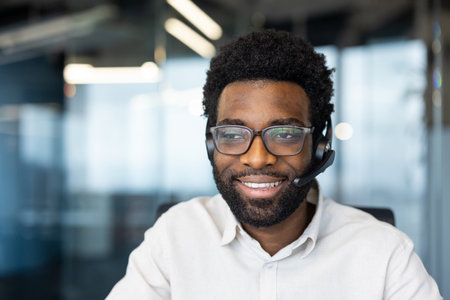 A cheerful man with glasses and a headset smiles, likely a customer service representative in a modern office setting.の写真素材