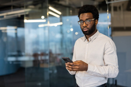 A serious-looking businessman wearing glasses, holding a phone in an office setting.の写真素材