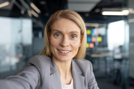 Successful woman looking into phone camera, talking to colleagues and partners using video call and smartphone app. Working inside office of modern building.の写真素材