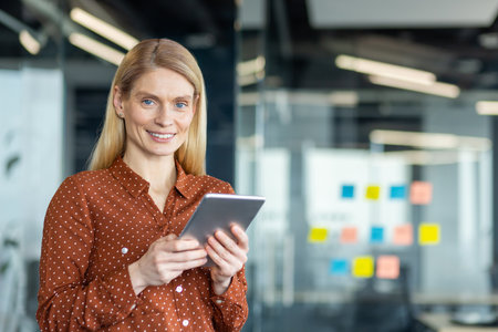 A smiling businesswoman in an office setting holds a tablet, ready for business.の写真素材
