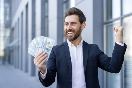 A successful businessman celebrates a financial achievement, holding cash with a triumphant...