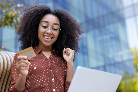 An excited woman holds a credit card while looking at her laptop, likely making an online purchase.